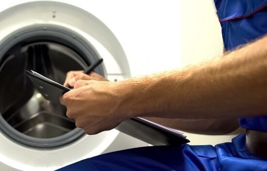 Appliance technician reviewing a repair checklist in front of a front-load washer